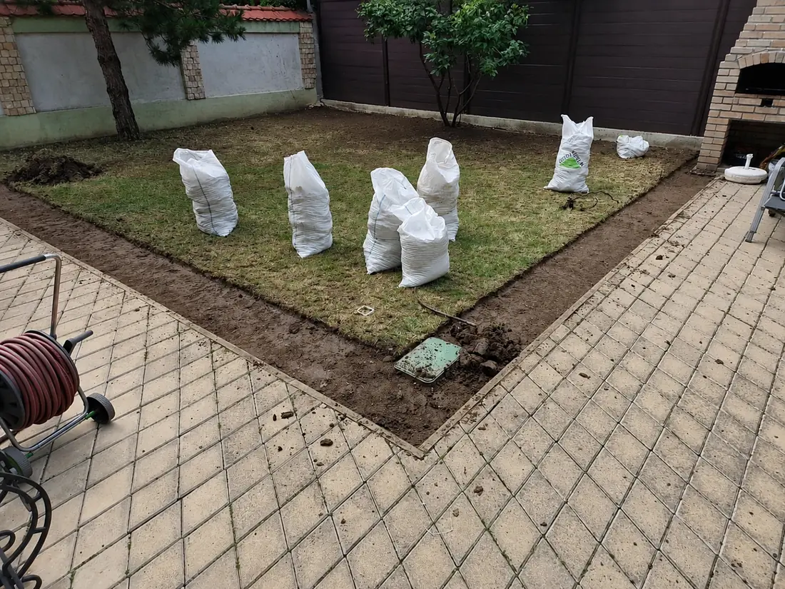Gazon vechi decopertat și strâns în saci albi, în mijlocul unei curți pavate, înainte de refacerea suprafeței