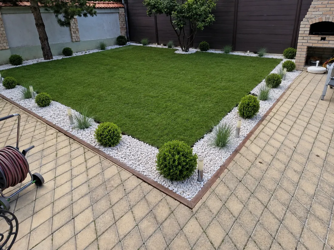Suprafață pătrată de gazon delimitată cu bordură de lemn și piatră albă, cu buxus tuns bilă, ierburi ornamentale și lămpi de grădină