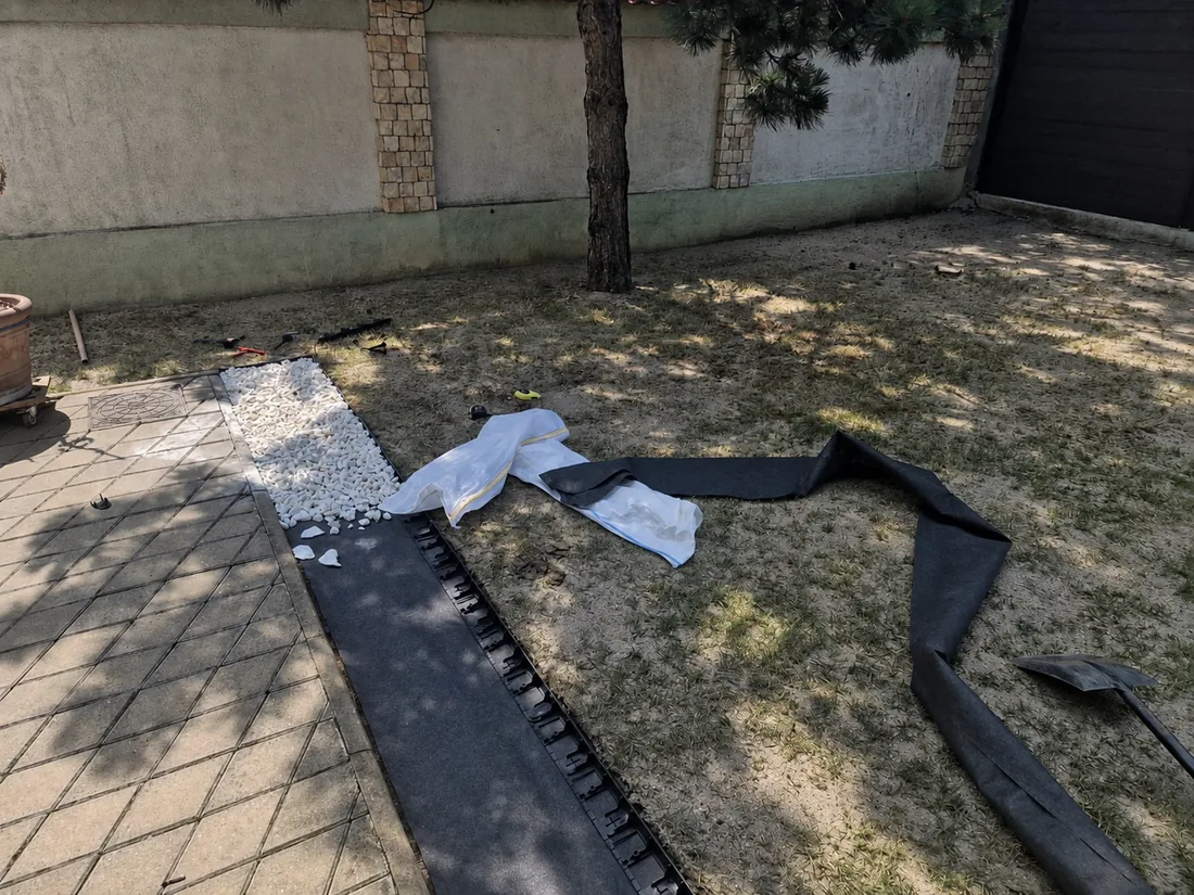 Lucrare în curs: bordură de delimitare montată pe marginea aleii, geotextil întins pe sol și piatră albă pusă pe prima porțiune
