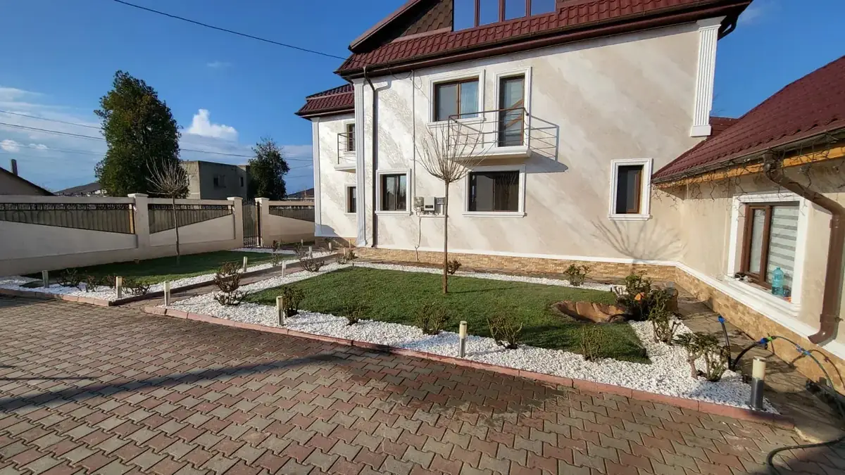 Grădină rezidențială finalizată în Buzău, cu gazon, borduri din piatră albă, trandafiri și iluminat de alee